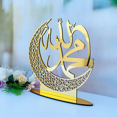 Decorative gold crescent moon with Arabic calligraphy on a white surface with flowers.
