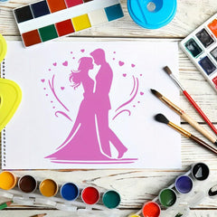 Painting of a couple in pink on a white paper with watercolor paints and brushes around.