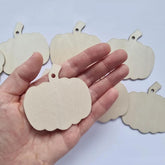 Hand holding a beige pumpkin-shaped tag with more tags on a light blue background