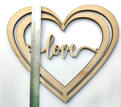 Wooden heart-shaped cutout with 'love' engraving and a ruler for scale on a white background