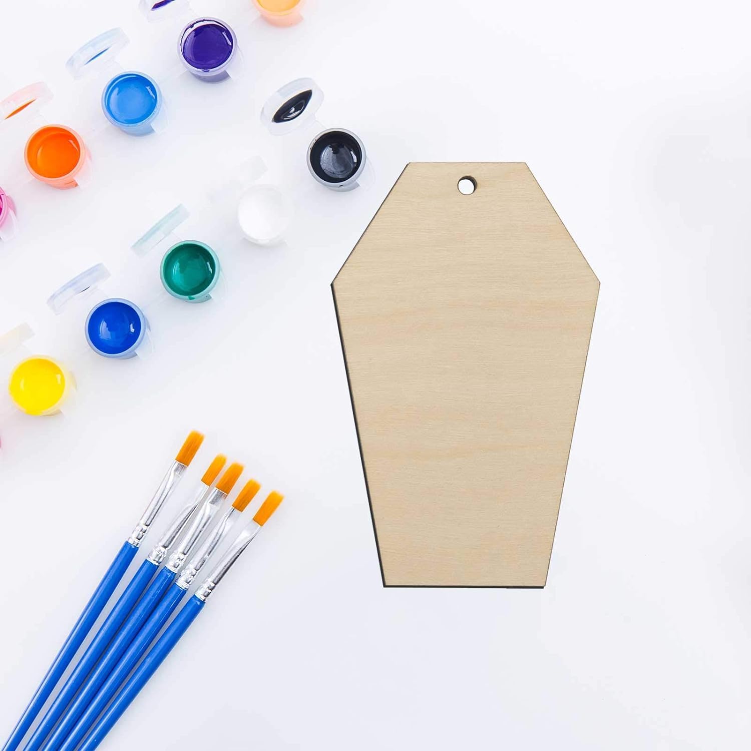 Wooden coffin-shaped craft board with paint supplies on a white background