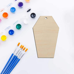 Wooden coffin-shaped craft board with paint supplies on a white background