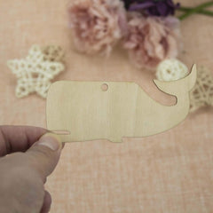 Wooden whale-shaped cutout held by a hand with flowers in the background