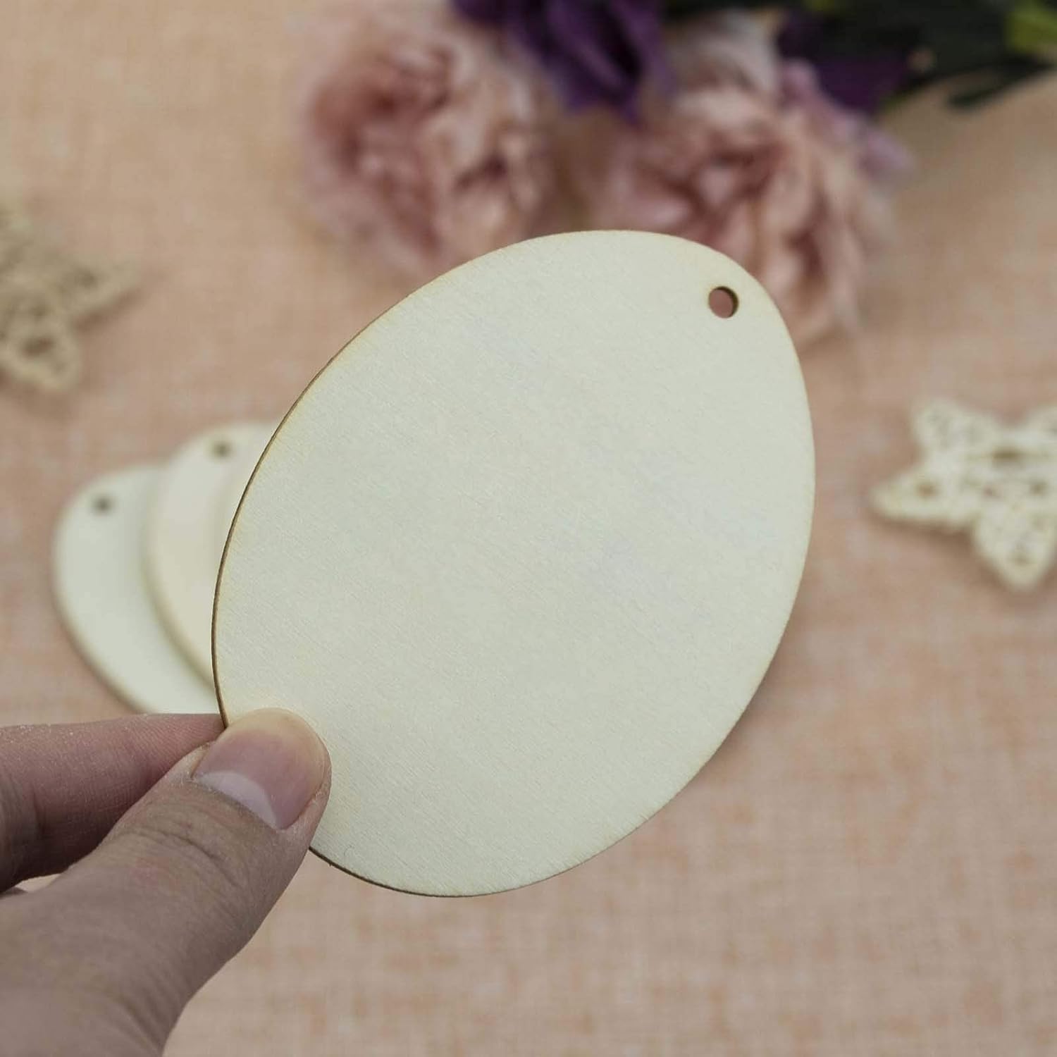 Hand holding a round wooden tag with floral and decorative items in the background