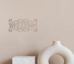 Decorative 'Welcome' sign on a beige wall with a white vase and box below.
