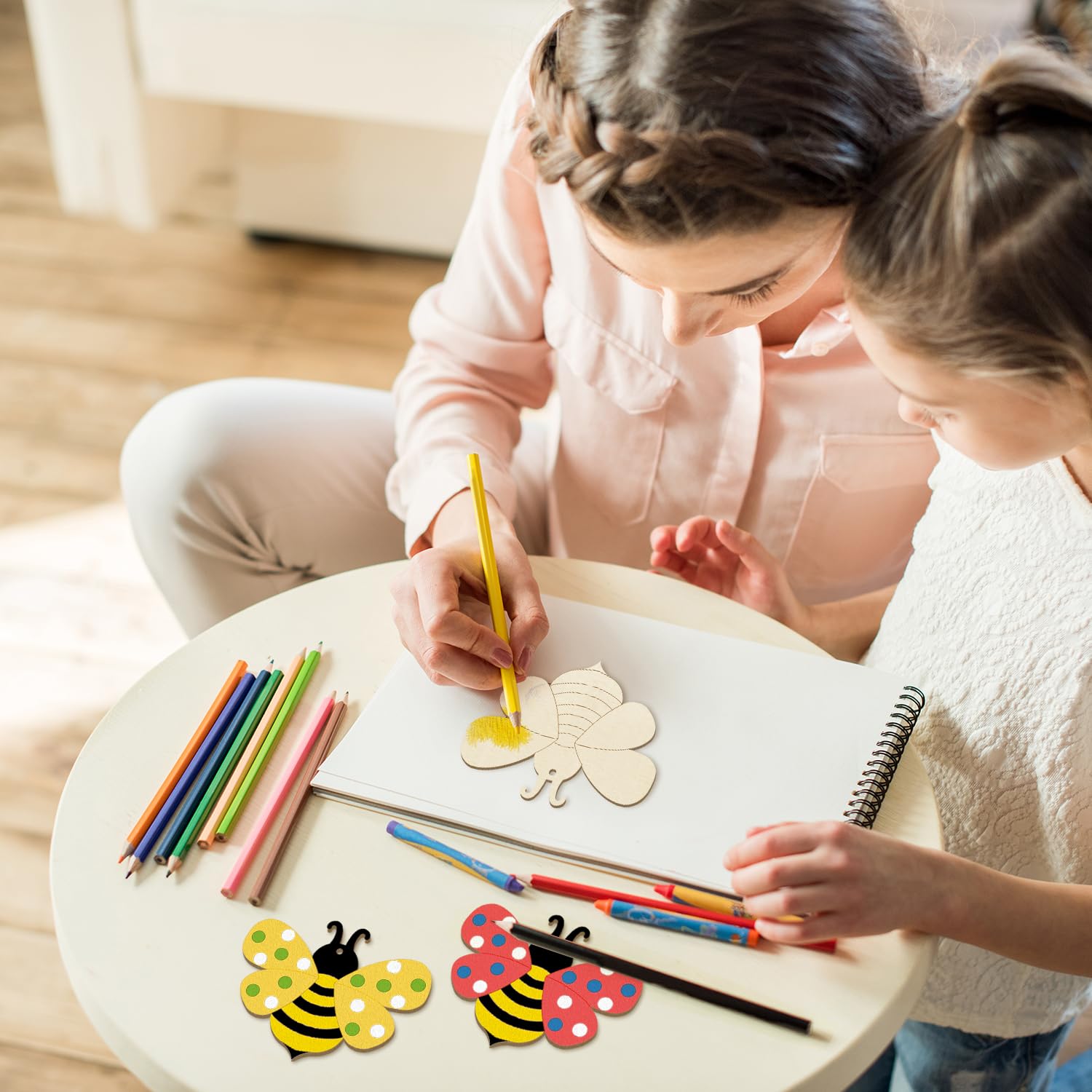 Two children sitting at a small round table with coloring materials, including crayons and paper.