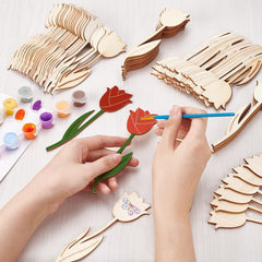 Hands painting wooden tulip shapes on a white surface with paint supplies.