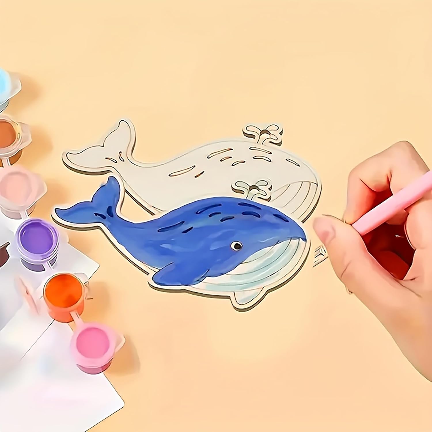 Hand painting a blue whale on a cardboard template with paint containers.