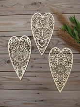 Three ornate heart-shaped wooden decorations on a wooden surface with greenery.