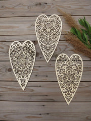 Three ornate heart-shaped wooden decorations on a wooden surface with greenery.