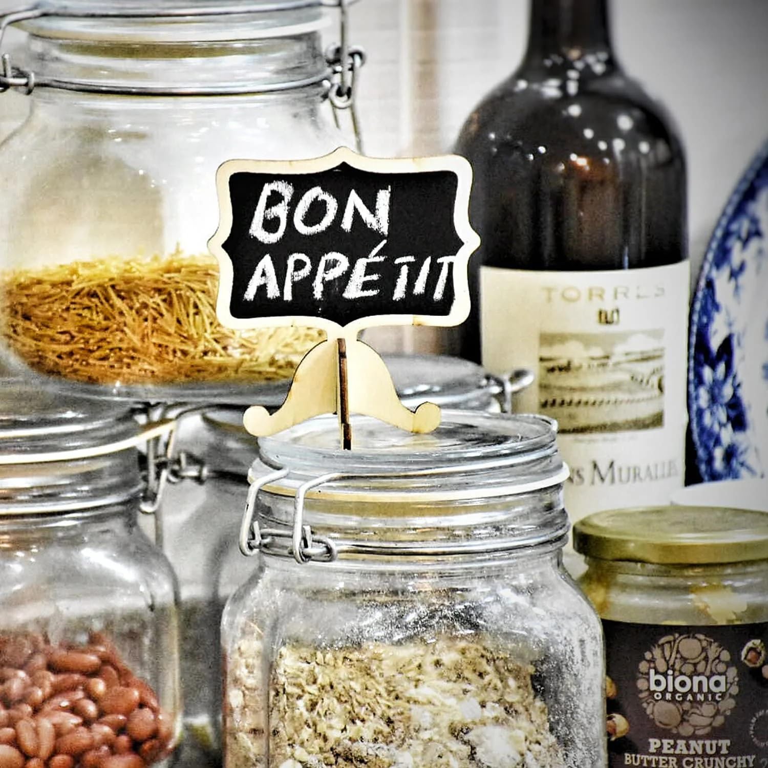 Glass jars with food ingredients and a 'Bon Appétit' sign in a kitchen setting.