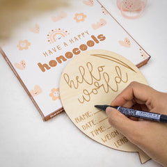 Wooden baby milestone board with 'hello world' text, being personalized with a marker.