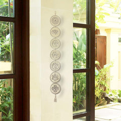 Decorative wall hanging with seven circular designs on a white wall with glass doors open to a garden.