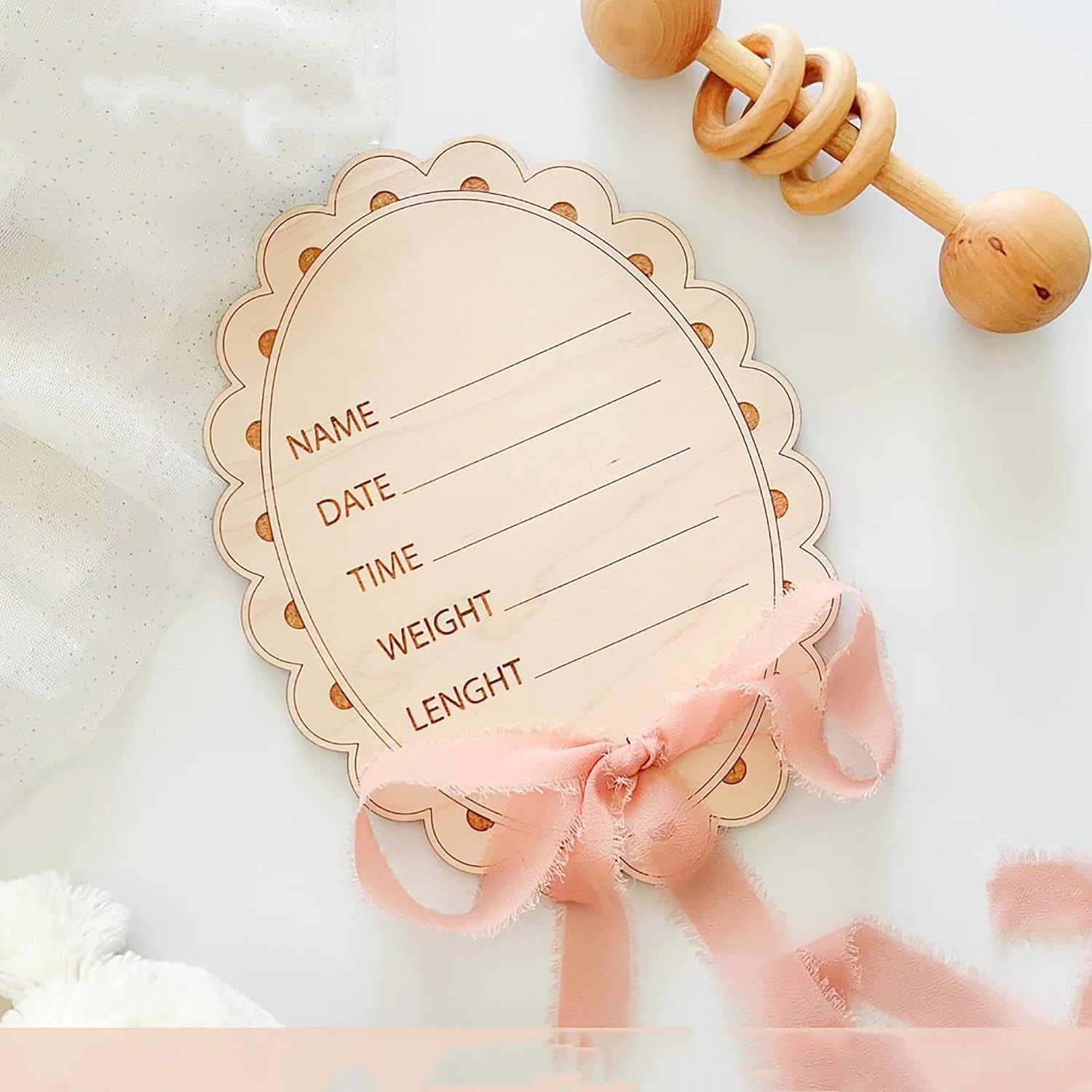 Wooden baby milestone card with decorative ribbon and wooden teething toy on a soft background