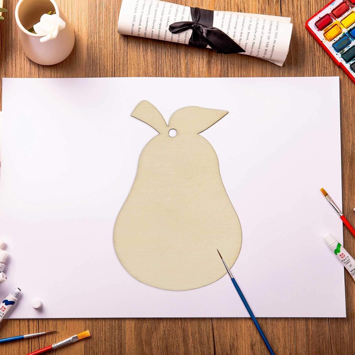 Paper cutout of a pear shape on a white sheet with art supplies on a wooden table.