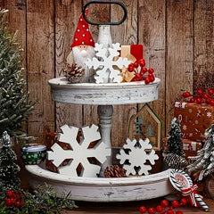 Decorative Christmas scene with a tiered stand, snowflakes, and festive decorations against a wooden background.
