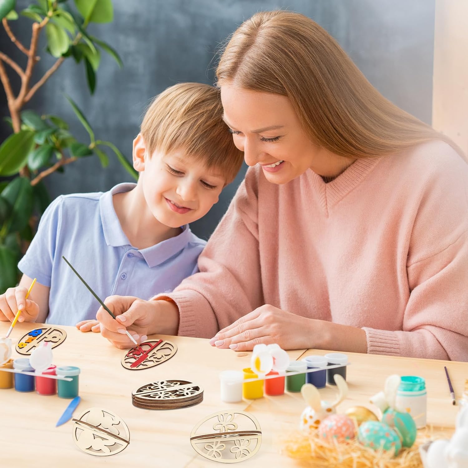 Woman and child painting decorative items at a table with art supplies.