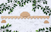 Decorative wooden cornice with floral design on a white marble background with green leaves.