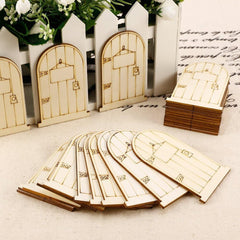 Wooden fairy doors on a textured surface with a white picket fence and greenery in the background.
