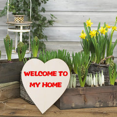 Heart-shaped sign with 'Welcome to My Home' text in a garden setting with plants and flowers.