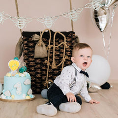 Child in formal attire with a decorated cake and balloons in a celebratory setting