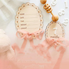 Baby milestone cards with wooden ribbons and decorative elements on a soft pink background