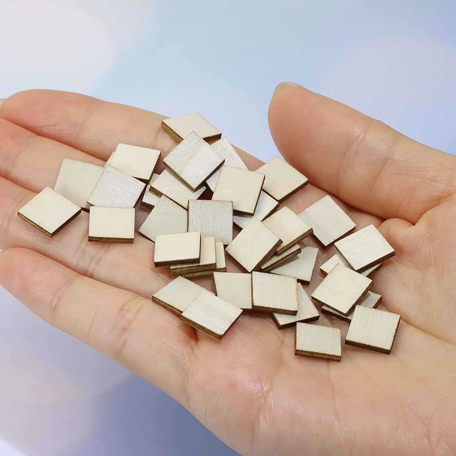 Hand holding a small pile of wooden square pieces against a light blue background
