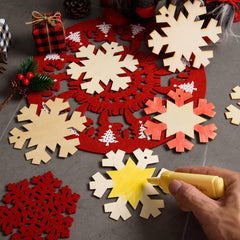 Decorative snowflake cutouts in red, white, and yellow on a gray surface with a hand holding a glue gun.