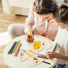Two children drawing on a wooden art easel with colorful pencils.