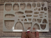 Metal template with cut-out shapes held by a hand on a wooden surface