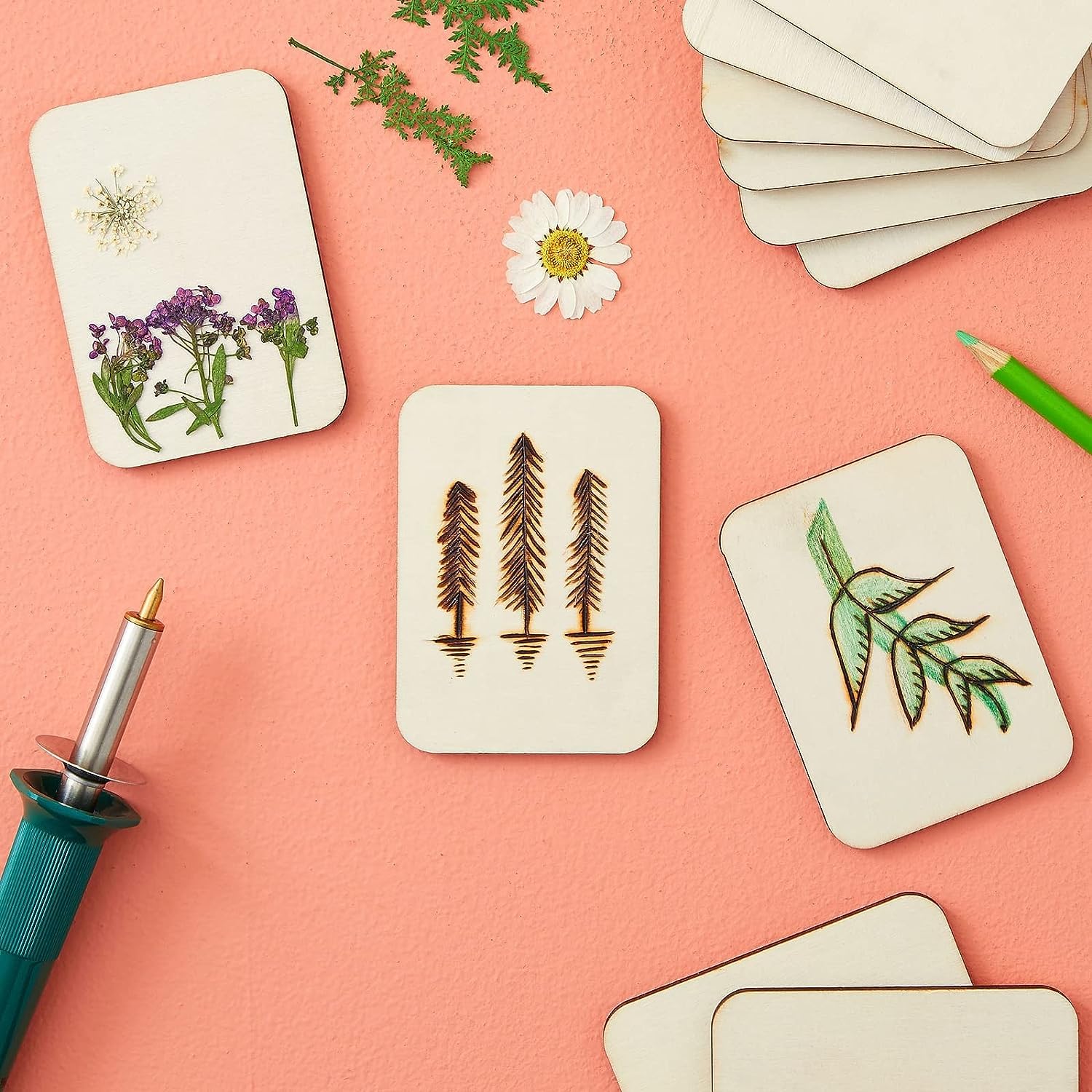Set of cards with nature-themed designs on a pink surface with a hot glue gun.