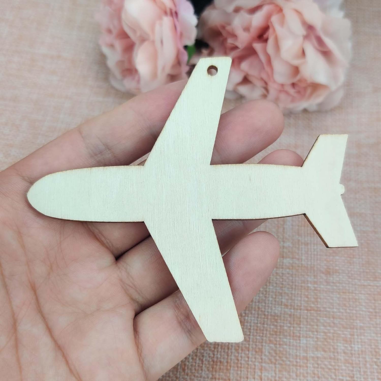 Wooden airplane-shaped ornament held in a hand with pink flowers in the background