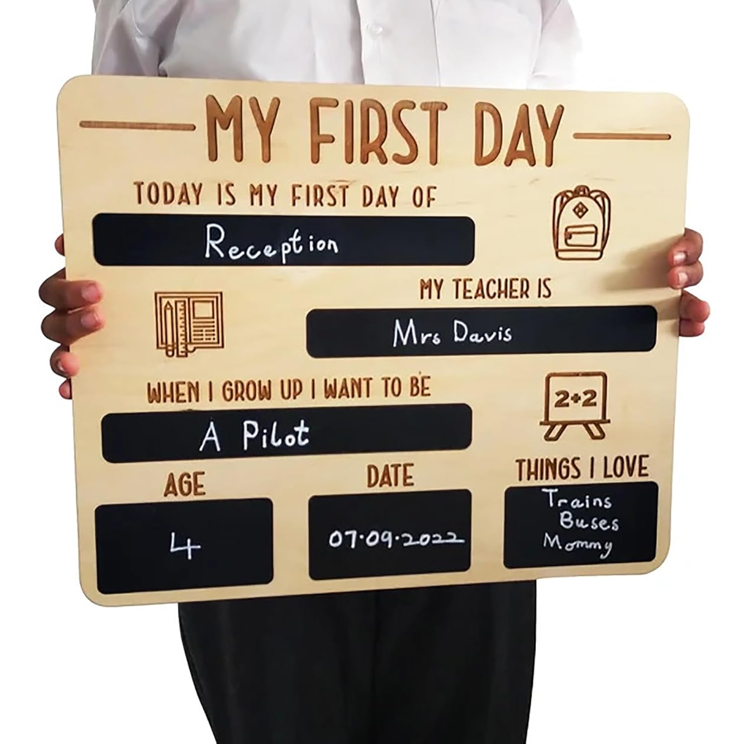 Wooden sign with chalkboard sections for a child's first day of school, held by a person.