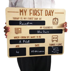Wooden sign with chalkboard sections for a child's first day of school, held by a person.