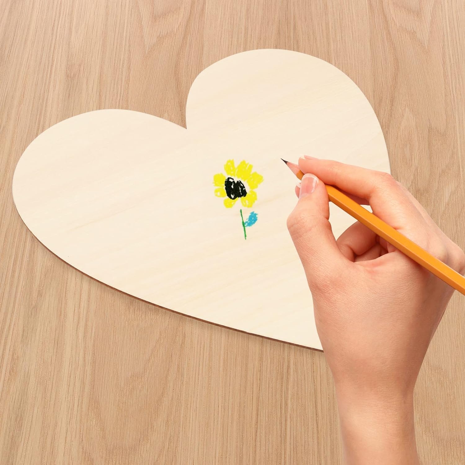 Hand drawing a flower on a heart-shaped piece of paper with a pencil.