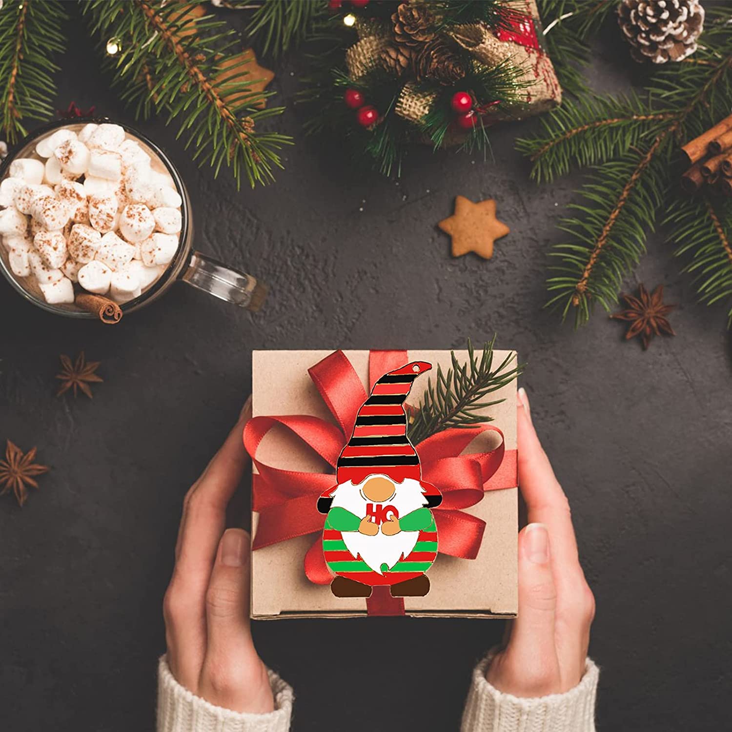 Person holding a small gift box with a gnome design on a festive background with a mug of hot chocolate and Christmas decorations.