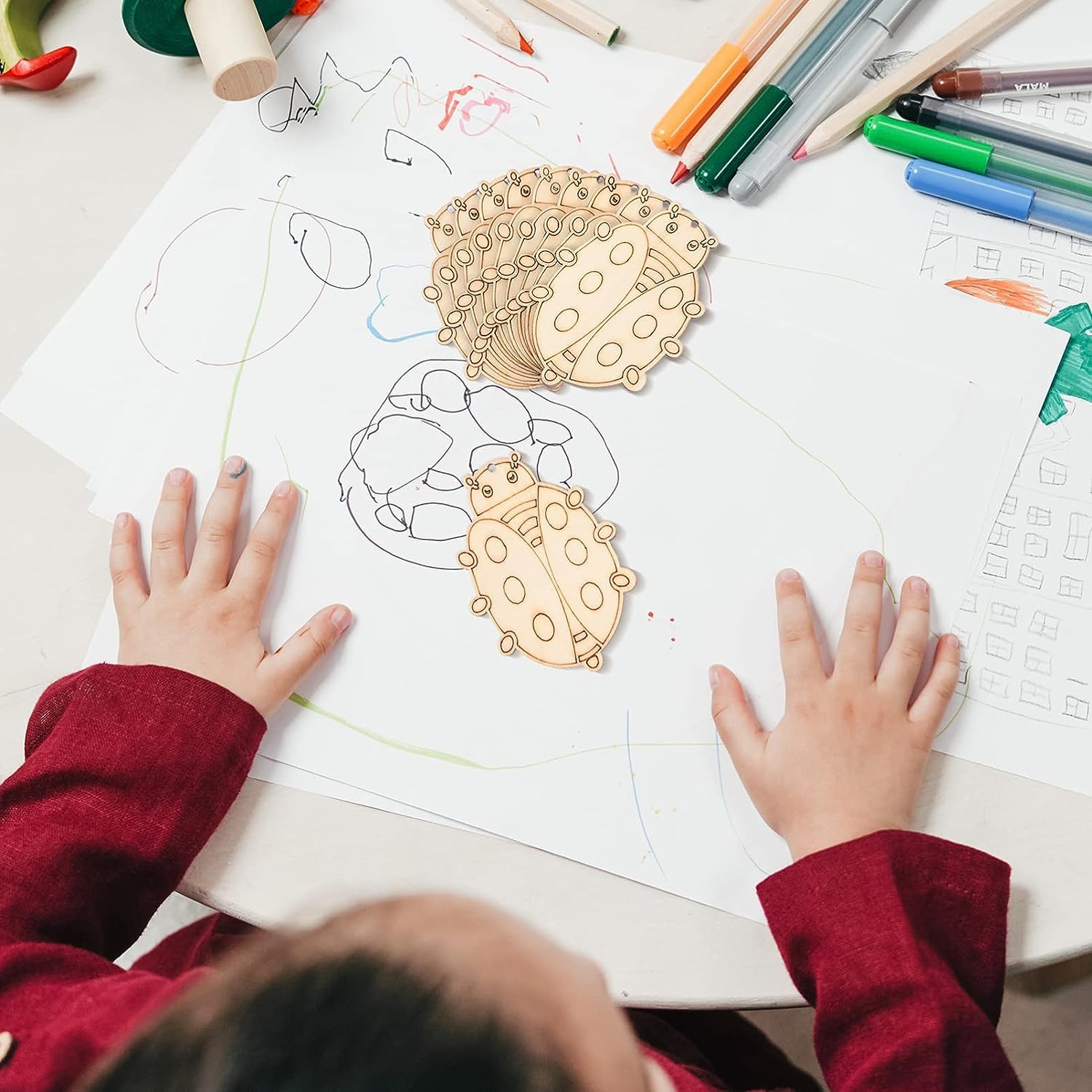 Child's hands on a coloring book with wooden ladybug shapes
