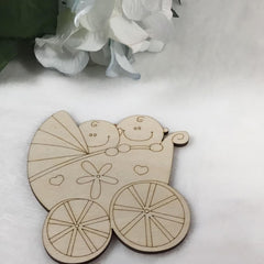 Wooden cutout of a baby carriage with two smiling babies on a white surface.