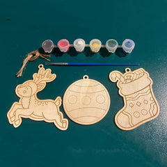 Wooden Christmas ornaments with paint supplies on a green surface