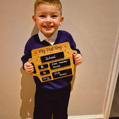 Child holding a wooden sign with 'My First Day of School' written on it, smiling.