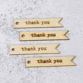 Four wooden tags with 'thank you' engraved on them, placed on a textured surface.