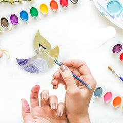 Person holding a paintbrush with watercolor paints and palettes on a white surface