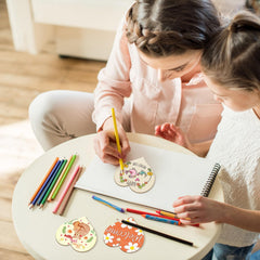 Two children sitting at a small round table coloring on paper with crayons.