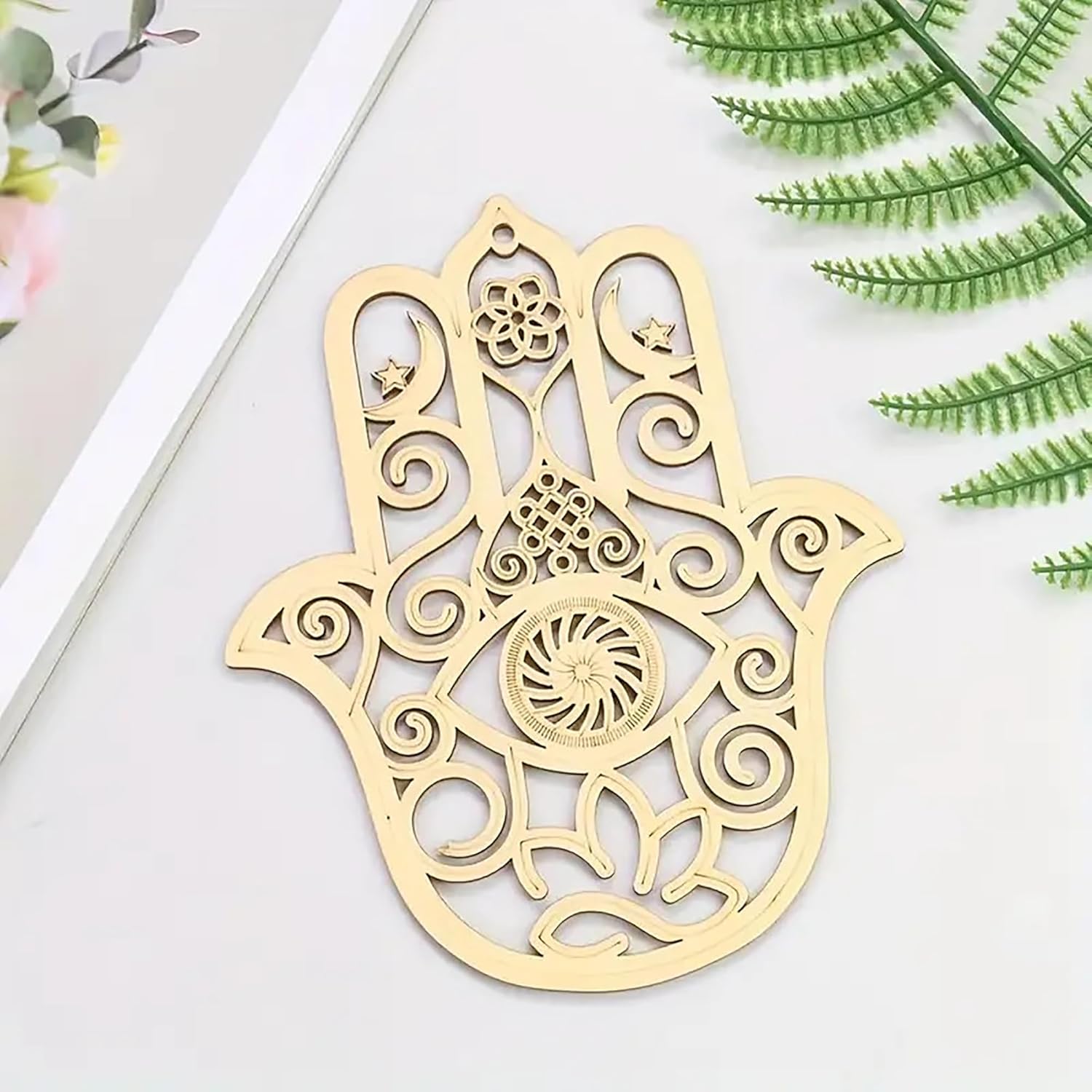 Decorative gold Hamsa hand on a white surface with green leaves in the background