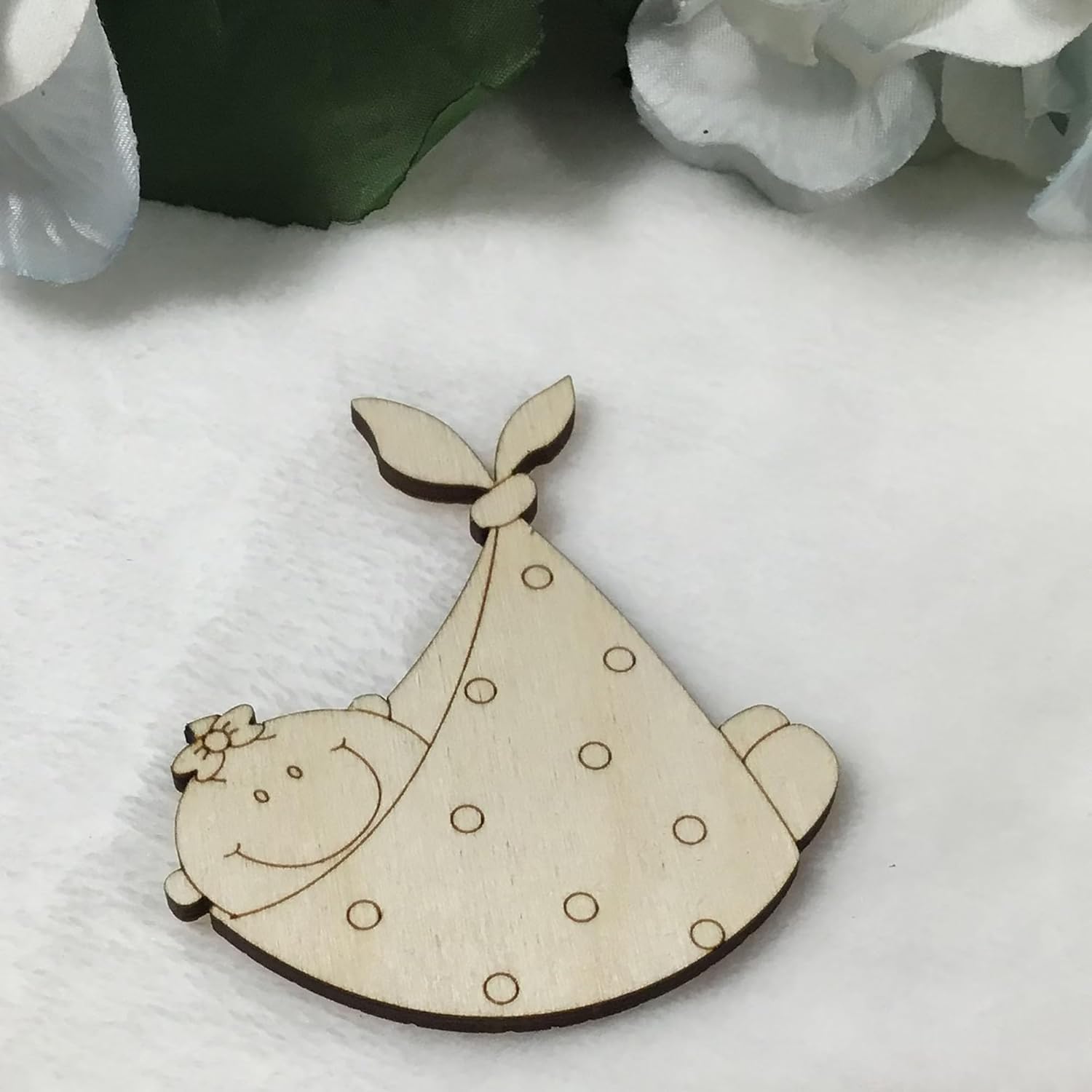 Wooden cutout of a baby in a crib with a white blanket on a light background