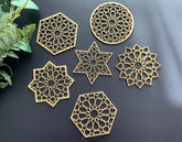 Set of gold geometric coasters on a dark surface with a plant on the side.