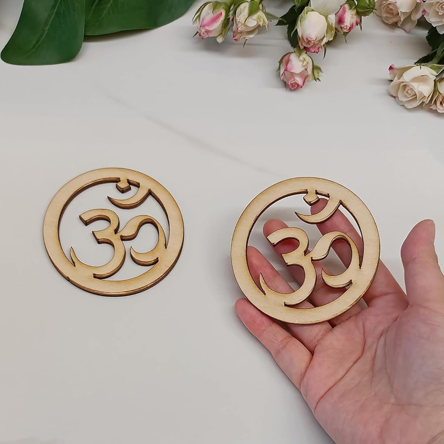 Two wooden coasters with Om symbol on a light surface with flowers in the background