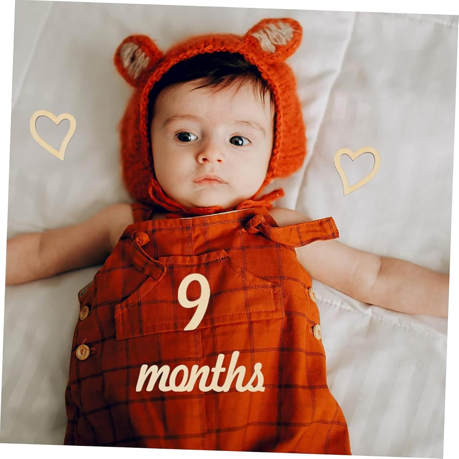 Baby wearing an orange outfit with '9 months' text and a matching hat with ears on a white background.
