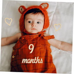 Baby wearing an orange outfit with '9 months' text and a matching hat with ears on a white background.
