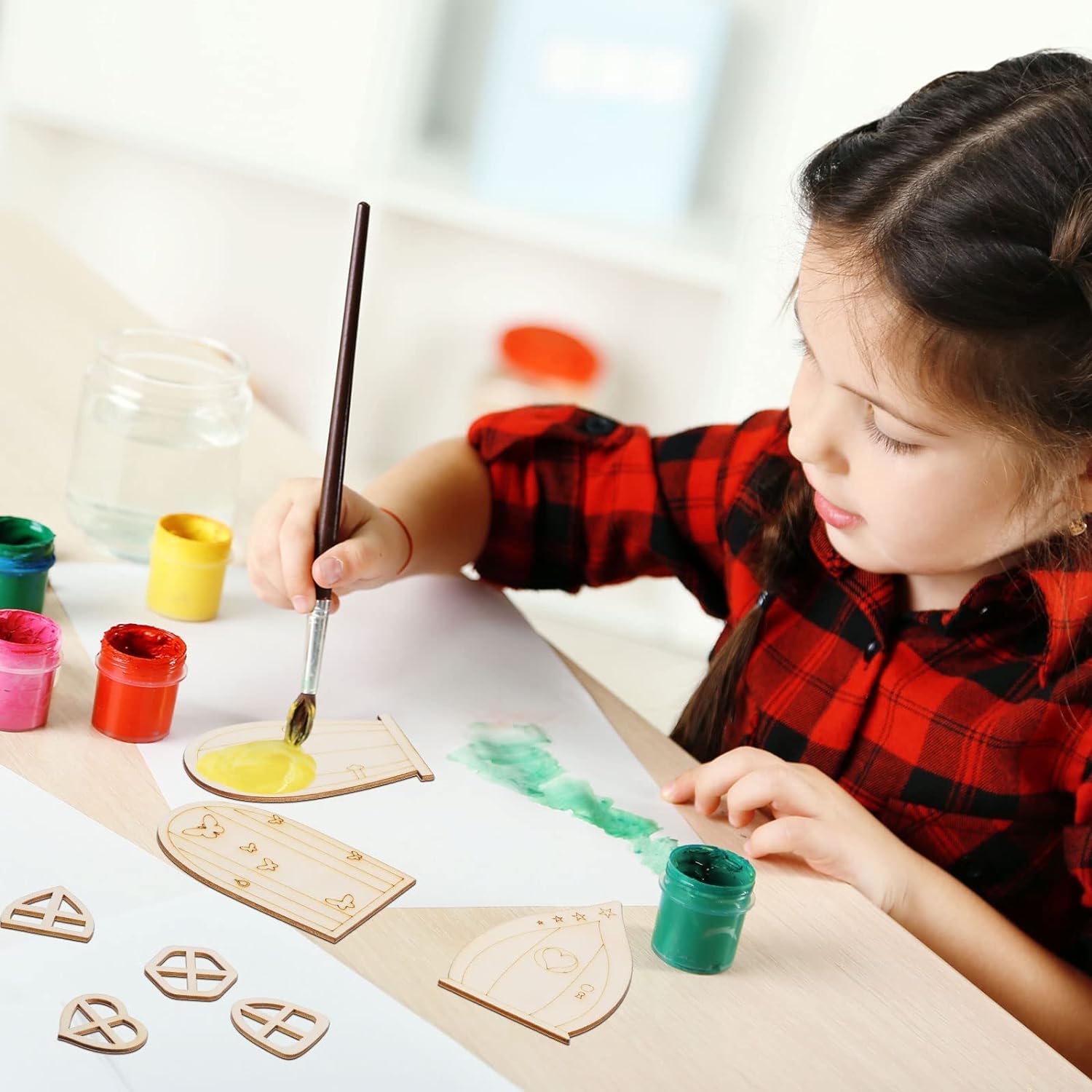 Child painting wooden shapes with colorful paint and a brush on a light surface.